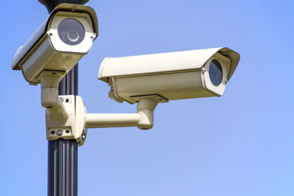 Two white CCTV cameras on a pole mount against a clear blue sky