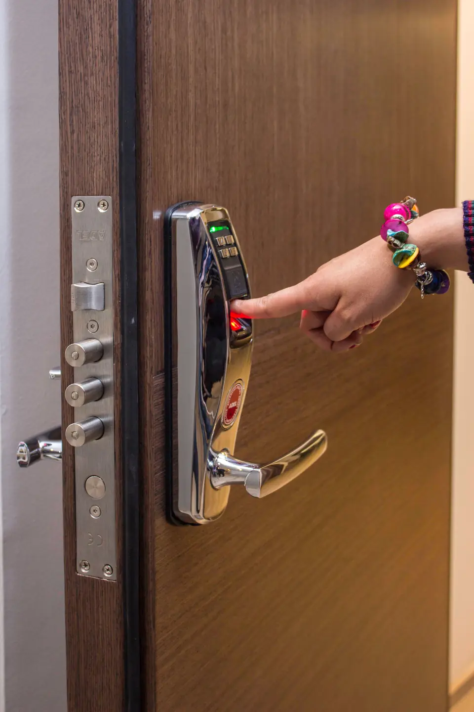A hand pressing the fingerprint reader on a chrome door lock