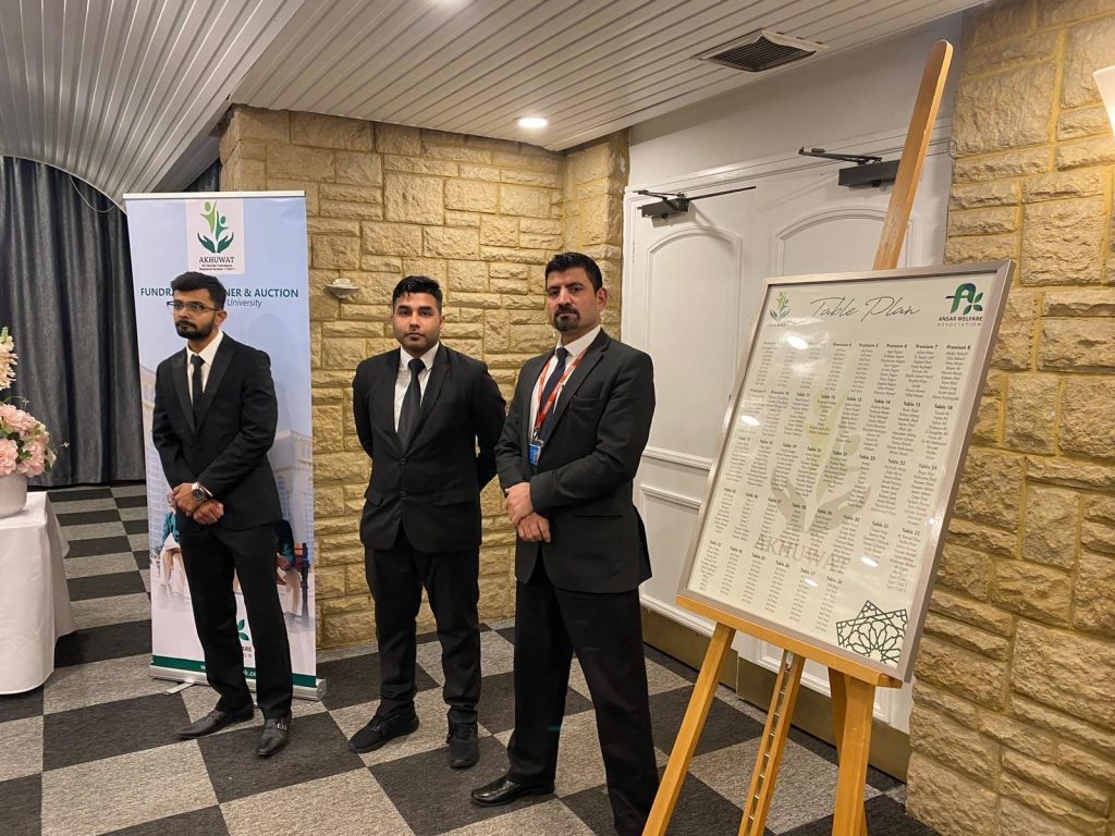 Three professional security guards from 2015 Security in black suits, standing at the entrance of a formal event next to the guest table plan.
